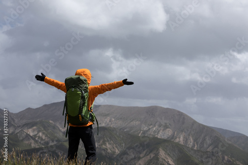 Successful woman backpacker open arms on high altitude mountain top