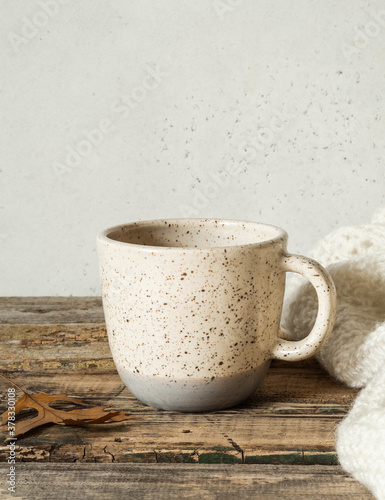 Two-tone mottled cup with a drink and a knitted blanket on an old wooden table