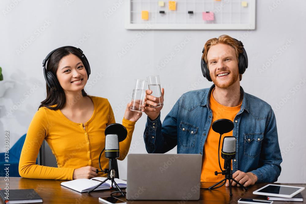 Φωτογραφία interracial couple of broadcasters in wireless headphones clinking glasses of wa