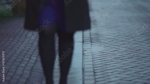 Woman walking towards, approaching on wet pavement. Gloomy Autumn day in rainy fall season. high angle leg concept shot of anonymity, loneliness depression and prostitution.