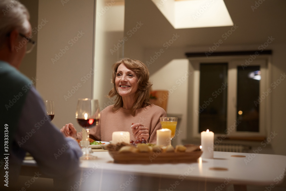Happy senior woman sitting at the table and talking to her husband during dinner at home