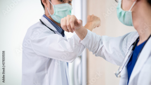 Two Asian professional doctors greeting each other with touching or bumping elbows instead of handshake, hug or kissing to avoid the spread of coronavirus. COVID-19 alternative handshake. © pitipat