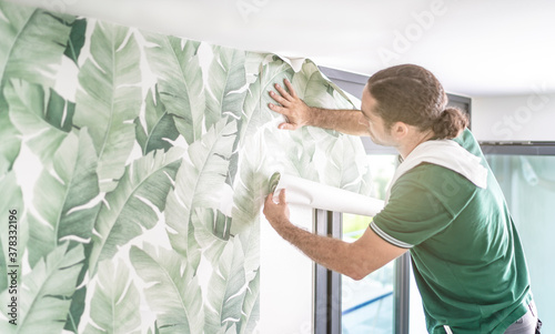 professioneller Tapezierer setzt eine frische Bahn Tapete an die bereits verklebte Mustertapete an photo