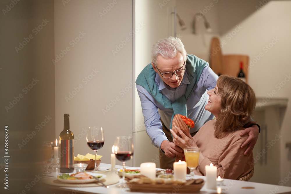 Senior man giving flowers to his wife during their romantic dinner in the kitchen Senior man giving flowers to his wife during their romantic dinner in the kitchen