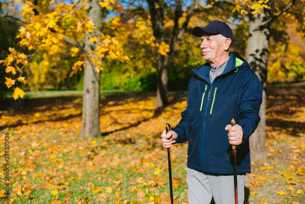 Smiling old man resting in autumn park after nordic walking. Senior athlete outdoors
