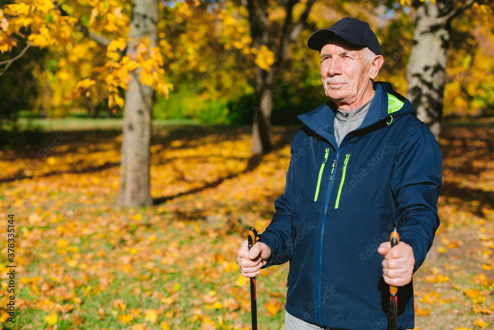 Old man resting in autumn park after nordic walking. Senior athlete outdoors