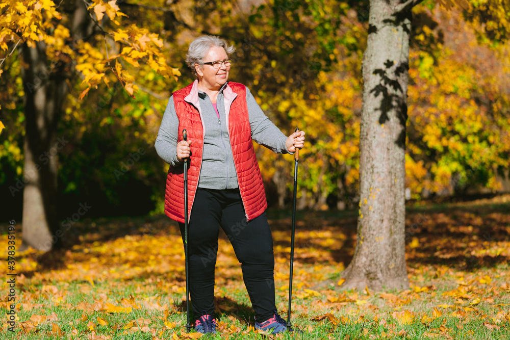 Old woman resting in autumn park after nordic walking. Senior athlete outdoors