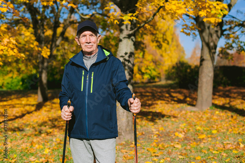 Obraz na płótnie Smiling old man resting in autumn park after nordic walking. Senior athlete outdoors w salonie