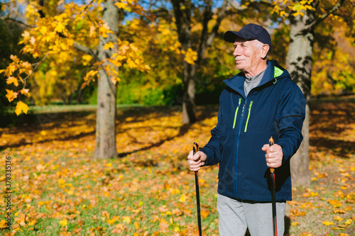 Obraz na płótnie Smiling old man resting in autumn park after nordic walking. Senior athlete outdoors w salonie