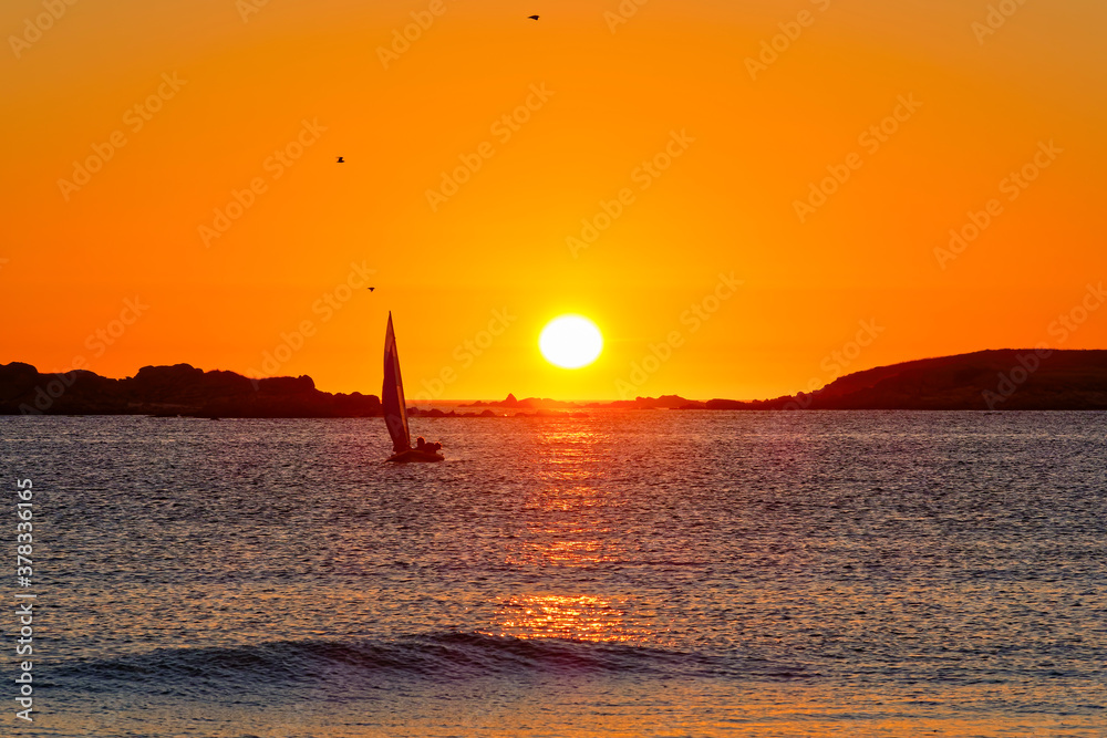 A lone yacht sails in the sunset off the brach at Landeda, Brittany