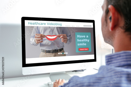 Back view of man using computer with health videoblog on the screen