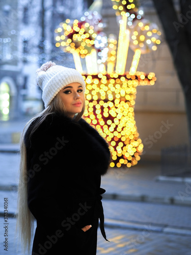 Obraz na płótnie Blonde girl posing at the winter city in a black fur coat and a white hat w salonie