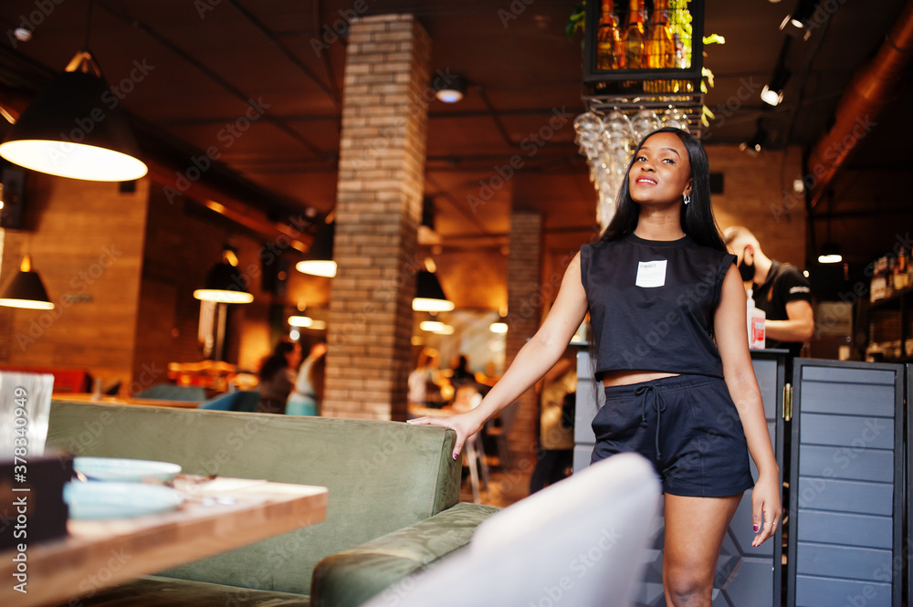 Fashionable feminist african american woman wear in black t-shirt and shorts, posed at restaurant. Fashionable feminist african american woman wear in black t-shirt and shorts, posed at restaurant.