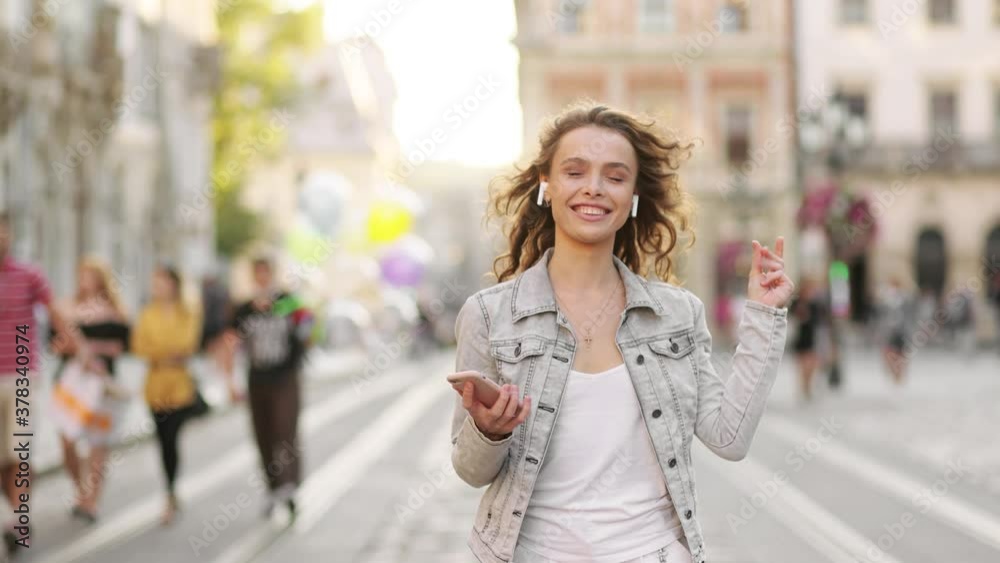 Happy woman having fun outdoor. A girl in the wireless headphones is dancing on the street. Beautiful smiling girl Happy woman having fun outdoor. A girl in the wireless headphones is dancing on the street. Beautiful smiling girl