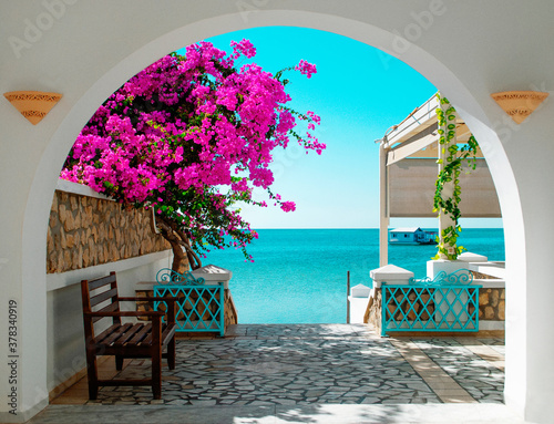 Fototapeta A view of the blue sea of ​​Tunisia through a white archway with pink blooming flowers in the foreground