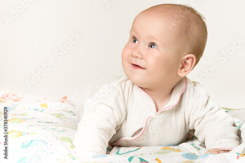 Adorable little girl, child aged six months, smiling happily at home lying on the crib. Family morning in a cozy home.