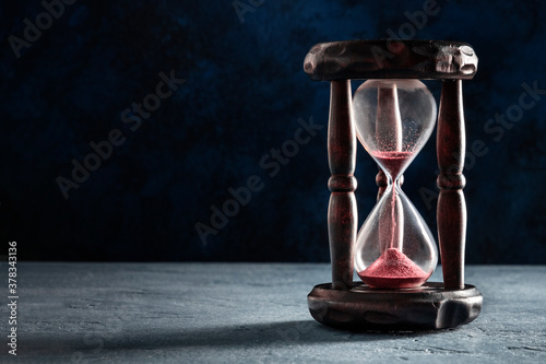 Time concept. An hourglass with sand falling through, on a dark background with copyspace