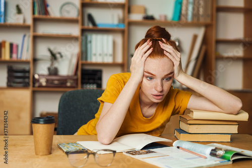 Fotografija Image of puzzled redhead girl doing homework while sitting at table