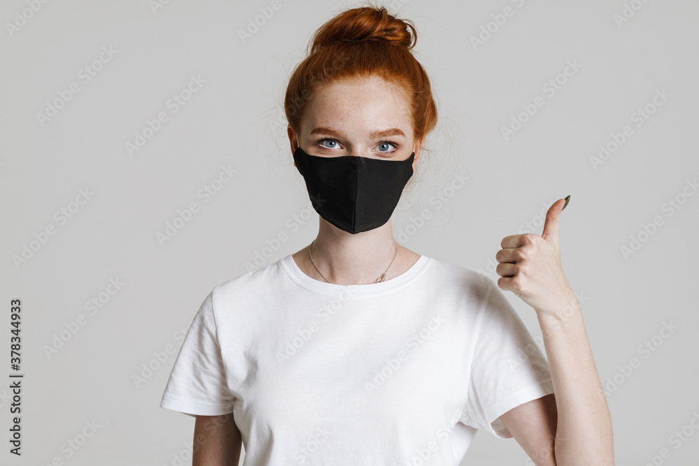 Photo of ginger beautiful girl in face mask showing thumb up Photo of ginger beautiful girl in face mask showing thumb up