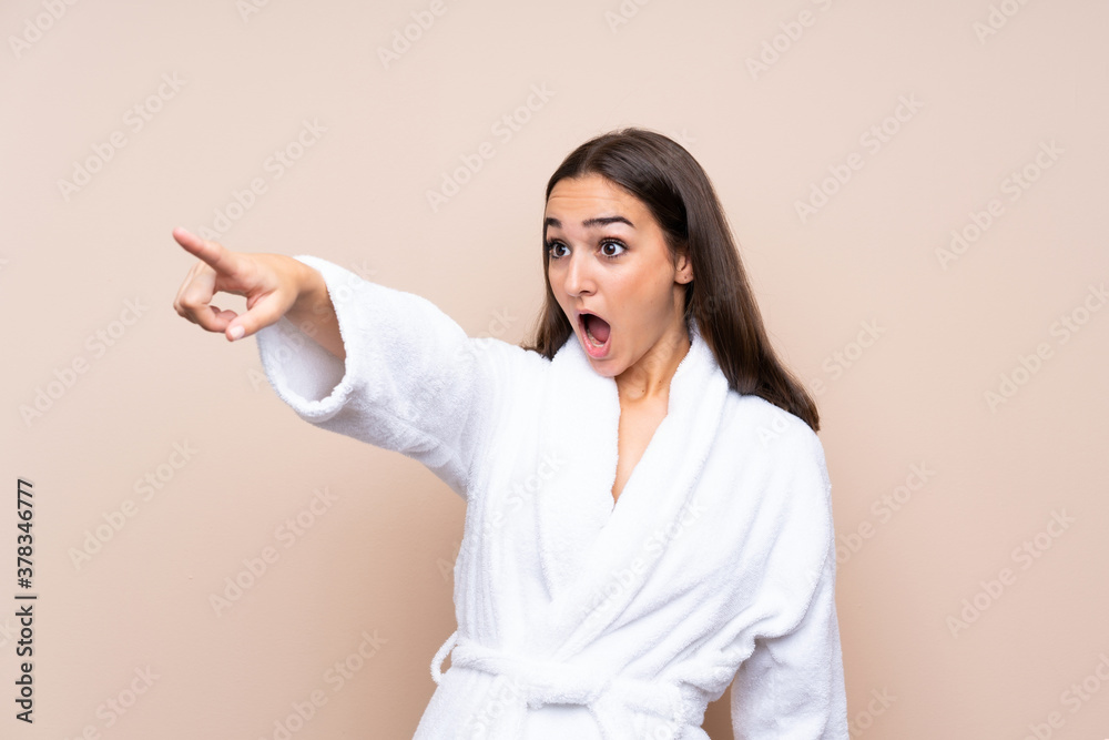 Young girl in a bathrobe over isolated background pointing away