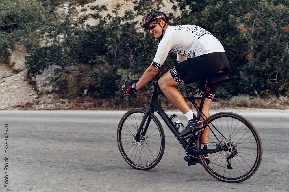 Obraz premium Man cyclist pedaling on a road bike outdoors in sun set