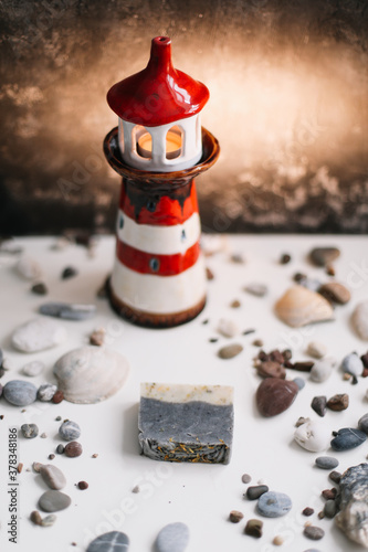 Small decorative lighthouse with sea shells and stones on dark background. Summer, holidays, vacation concept. Flat lay, top view