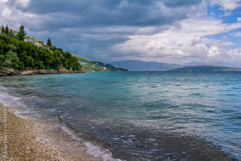 Beautiful landscape - turquoise colored sea water, golden sand, gray sky with dark stormy clouds and mountains on the horizon.