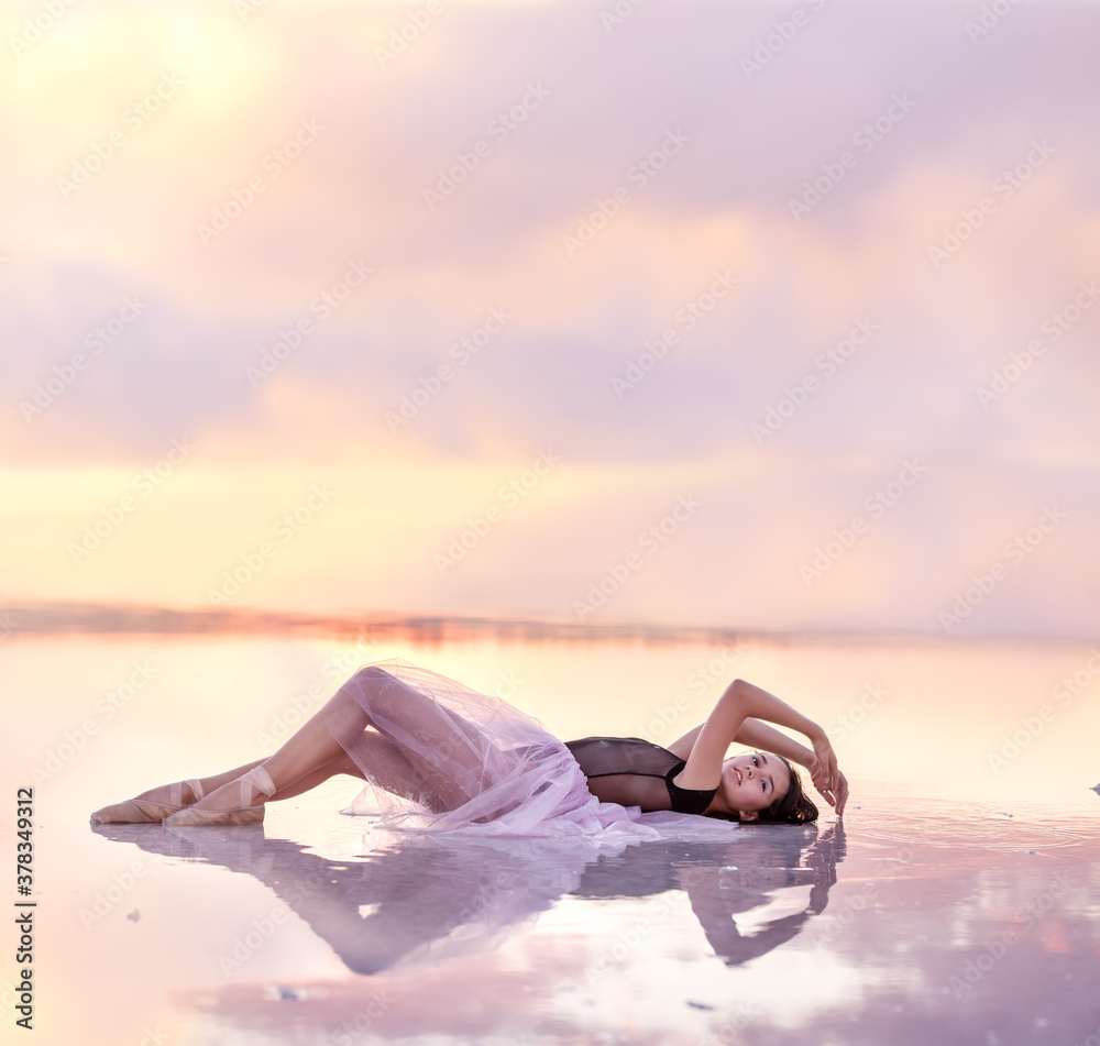 A young girl in an airy dress lies in the water of a pink lake. Artistic gentle magical photo.