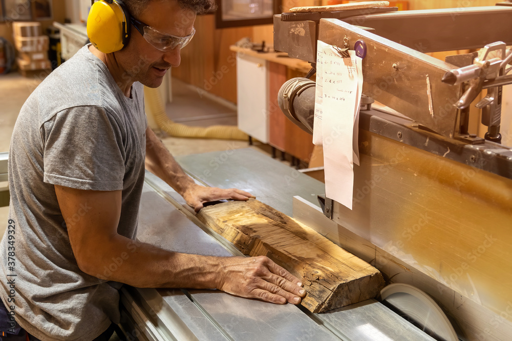 Carpenter cutting wood with a machine wearing earplugs - obrazy, fototapety, plakaty 