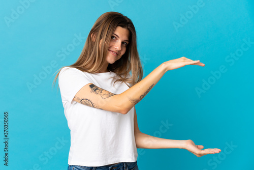 Young slovak woman isolated on blue background holding copyspace to insert an ad