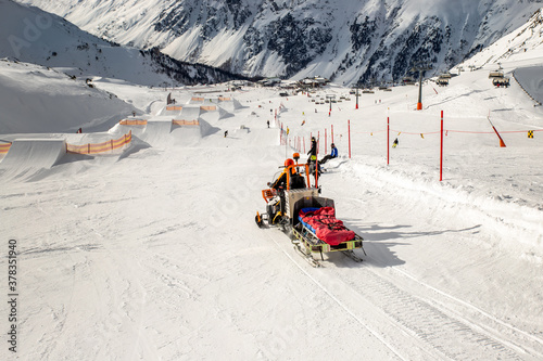 Snowmobile machine with sled and equipment riding fast hurry up driver to help injured skier or snowboarder at accident on winter mountain resort. Emergency rescue vehicle at ski slope piste downhil photo