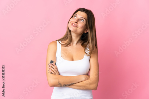 Young slovak woman isolated on pink background looking up while smiling