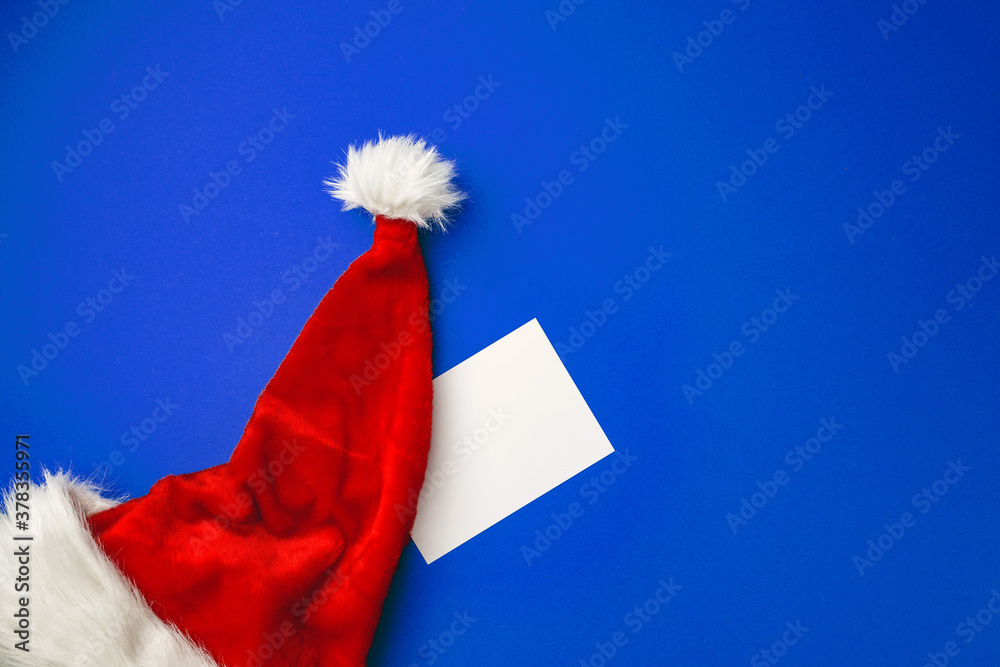 Blank paper sheet and Snata Claus hat on blue background