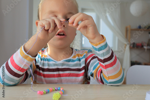 Little girl is making bracelet from beads