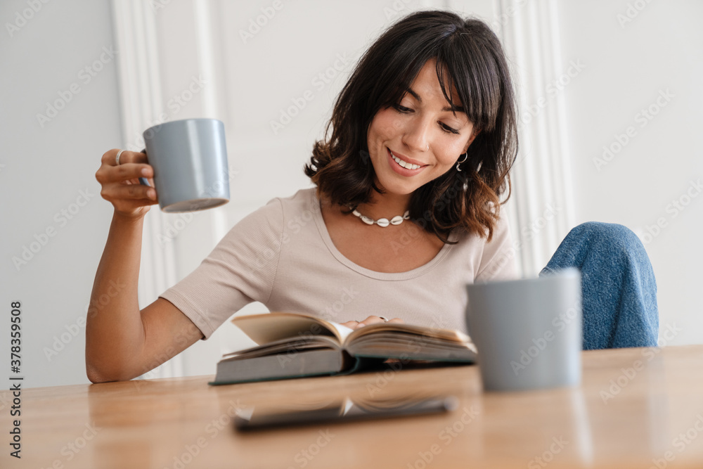 Image of smiling beautiful woman reading book while drinking coffee Image of smiling beautiful woman reading book while drinking coffee