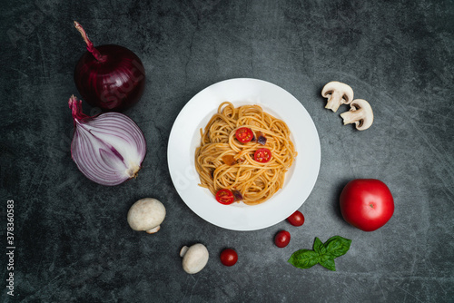A plate of spaghetti and ingredients on a dark gray background