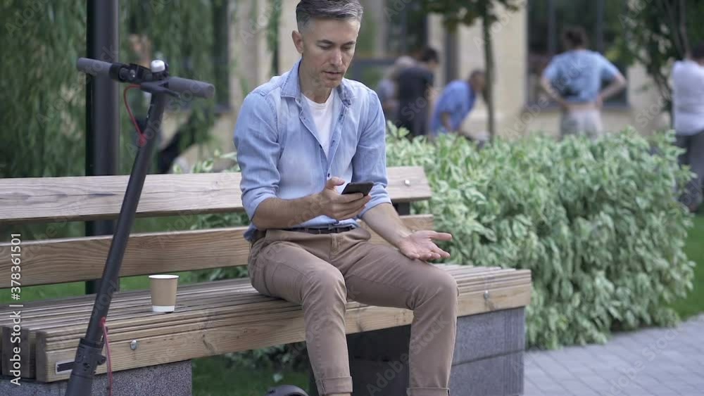 Adult man sitting on the bench, holding mobile phone. Reading bad news and breaking mobile. Slowmotion. Adult man sitting on the bench, holding mobile phone. Reading bad news and breaking mobile. Slowmotion.