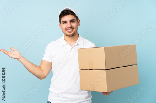 Delivery caucasian man isolated on blue background holding copyspace imaginary on the palm