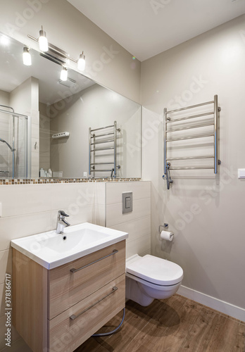 Modern interior of bathroom in luxury apartment. Sink with wooden drawers. WC toilet. Hardwood floor.