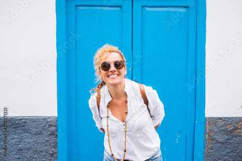 Portrait of cheerful and beautiful adult young caucasian woman smile and have fun in front of the camera and with blue door and white wall in background - home and people outdoor concept lfe photo
