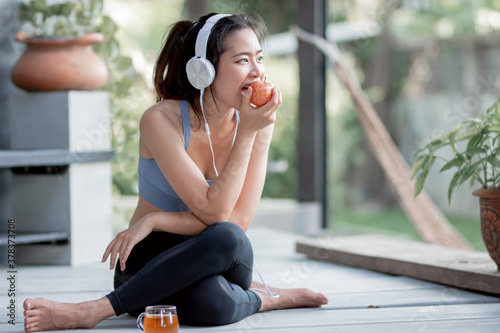 Healthy and Sportive woman eating apple and using headphone to listen music photo