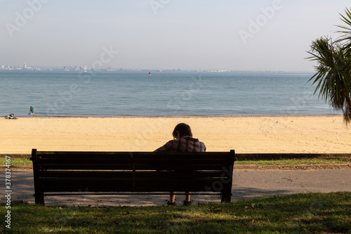 a woman sitting alone on a bench at the seaside or beach
