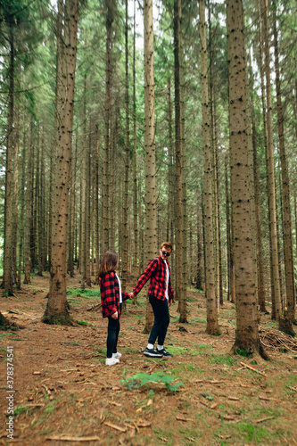 Young couple in red shirts walking in the wild forest holding hands. Couple of tourists in a forest hike holding hands. Vertical