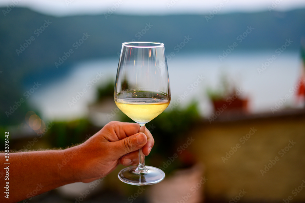 Obraz premium Hand with glass of cold dry white wine served outdoor in cafe at night in Italy