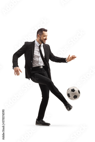 Full length shot of a man in suit and tie kicking a football