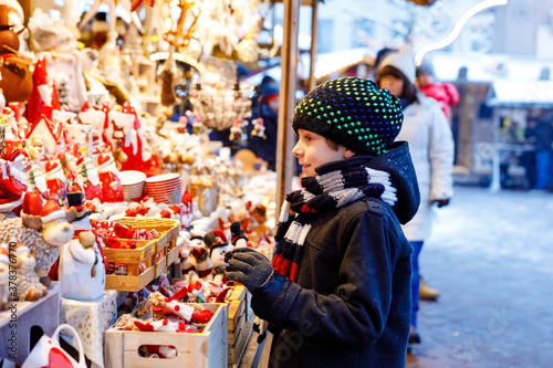 Little cute kid boy selecting decoration on Christmas market. Beautiful child shopping for toys and decorative ornaments stuff for tree. Xmas market in Germany.