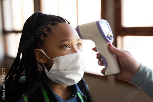 Girl wearing face mask getting her temperature measured in class at school photo