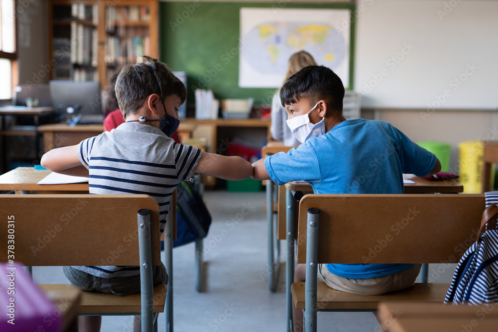 Two boys wearing face masks greeting each other by touching elbows at school Two boys wearing face masks greeting each other by touching elbows at school