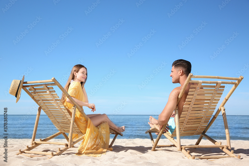 Woman and her boyfriend on deck chairs at beach. Happy couple