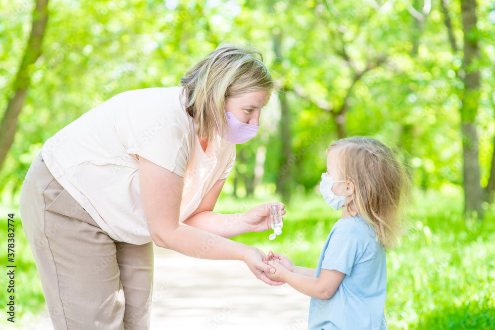 Woman wearing protective face mask applies sanitizer for cleaning baby hands Woman wearing protective face mask applies sanitizer for cleaning baby hands